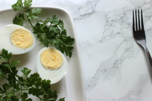 Boiled chicken egg and parsley on a white plate on a marble background.