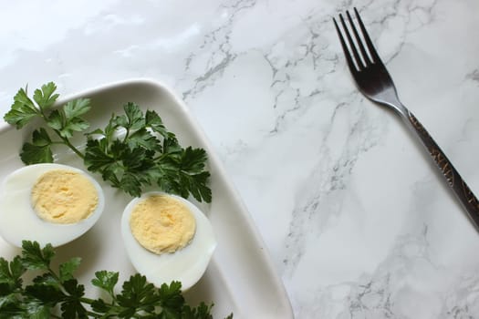 Boiled chicken egg and parsley on a white plate on a marble background.