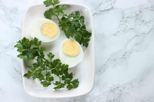 Boiled chicken egg and parsley on a white plate on a marble background.
