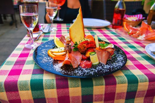 Traditional Italian food. Close-up of mixed Mediterranean appetizers or antipasto and tapas with ham vegetables and crab on black plate on restaurant table.