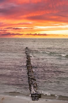 Groynes jut out into the Baltic Sea. Sunset on the horizon. Wooden logs protecting the coast. Landscape from the sea