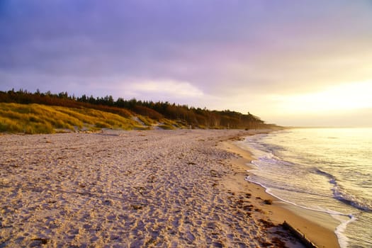 Sunset on the west beach on the Baltic Sea. Waves, beach, cloudy sky and the last rays of sunshine on the coast. Landscape photo