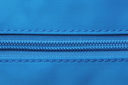 Zip fastener background texture. A high-resolution close-up of a detail from a closed plastic zip fastening on a backpack made of an elastic blue nylon fabric. Macro photo.