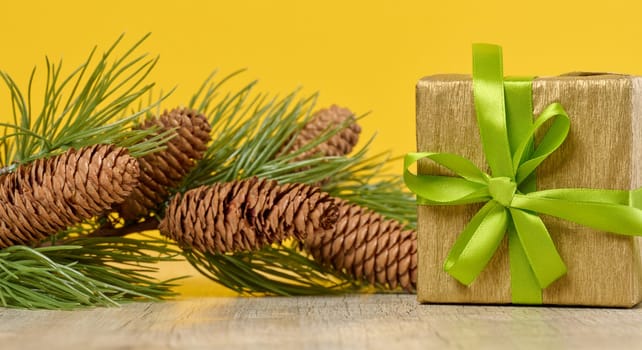 Box with a gift and a spruce branch with cones on a yellow background