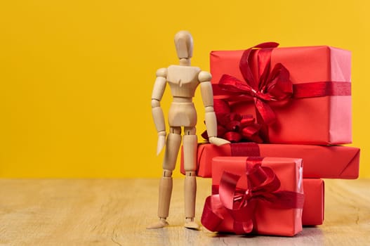 Stack of gifts and wooden mannequin on yellow background, holiday