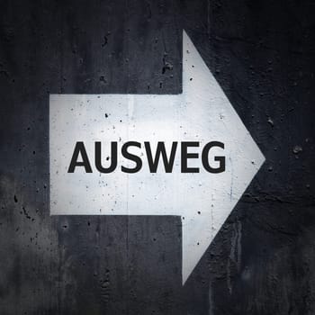 white directional arrow on a concrete wall with the German inscription Ausweg. Translation: way out
