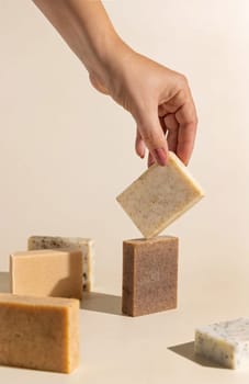Hand keeps natural beige and brown soap bars on light beige, close up, hard shadows. Hygiene products for Spa and skin care. Using organic handmade soap in everyday routine