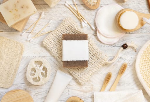 Organic handmade beige soap bar with blank label on soap saver bag near hygiene Items - natural sponges and brush, bamboo toothbrushes and cotton swabs, top view, mockup