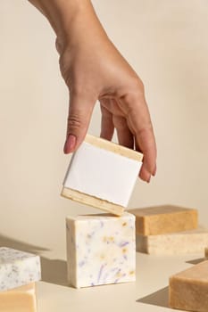 Hand keeps natural beige soap bars with blank label on light beige, close up, hard shadows. Hygiene products for Spa and skin care. Using organic handmade soap in everyday routine