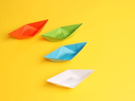Four different paper boats on a yellow background, teamwork concept