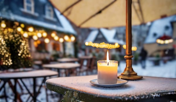 A solitary candle burns brightly on a frost-covered table, its flame a beacon of warmth against a snow-dusted café backdrop, adorned with festive lights