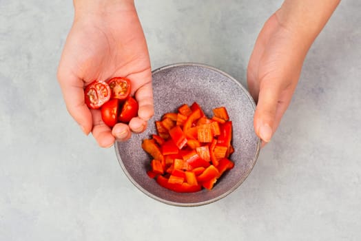 Tomatoes and red sliced pepper pieces in a bowl, prepare healthy food with paprika vegetables, holding fresh organic nutrition in the hands