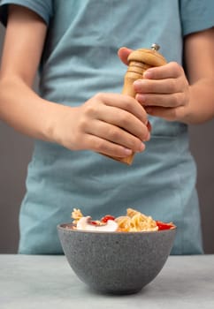 Putting pepper in a pasta salad, sliced mushroom, tomato, red pepper pieces and tuna, healthy food with vegetables, fresh organic nutrition
