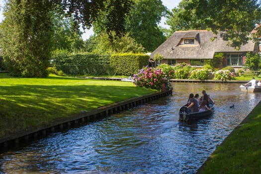 GIETHOORN, THE NETHERLANDS - AUGUST 05, 2015: Unknown visitors in the sightseeing boating trip in a canal in Giethoorn. The beautiful houses and gardening city is know as "Venice of the North""."