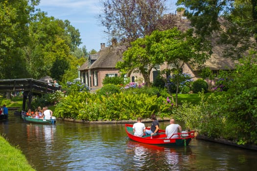 GIETHOORN, THE NETHERLANDS - AUGUST 05, 2015: Unknown visitors in the sightseeing boating trip in a canal in Giethoorn. The beautiful houses and gardening city is know as "Venice of the North""."