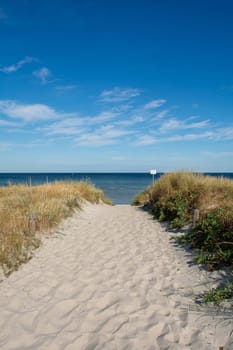 Path between the sand dunes overlooking the sea with blue sky. With sign "Grones - Please keep your distance - risk of accident"""