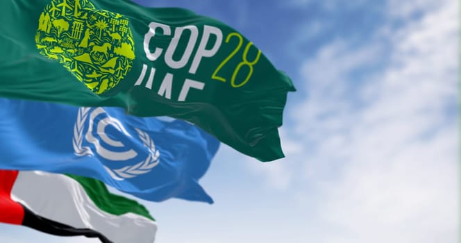Dubai, UAE, Nov. 30 2023: Flags of COP28, UNFCCC and UAE waving on a clear day. 3d illustration render. Selective focus. Rippling fabric