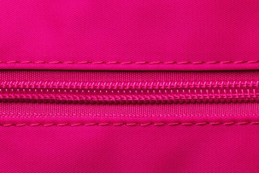 Zip fastener background texture. A high-resolution close-up of a detail from a closed plastic zip fastening on a backpack made of an elastic pink nylon fabric. Macro photo.