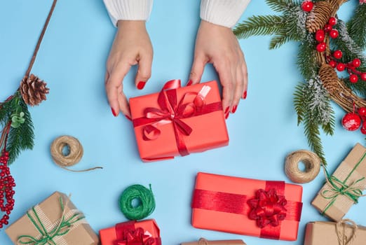 Woman is packing gifts, the pre-holiday bustle and preparations for Christmas. Gifts wrapped in red paper and tied with ribbon