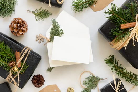 Paper card between Christmas decor, black gift boxes and green fir branches top view. horizontal blank card mockup, flat lay, copy space. Christmas or New Year Holiday greeting card