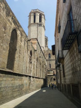 Visitors walking by narrow lanes of Barcelona Gothic  Quarter. Cathedral Bell Tower at bottom