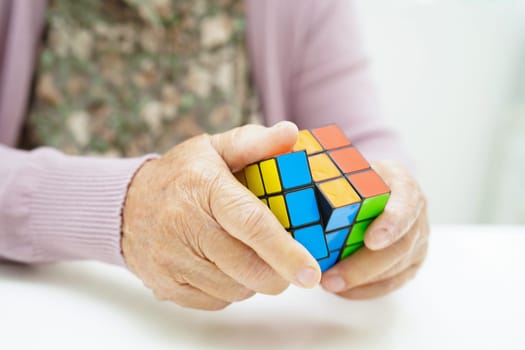 Bangkok, Thailand - May 15, 2022 Asian elderly woman playing Rubik cube game for treatment dementia prevention and Alzheimer disease.