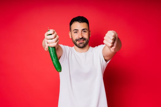 Male hand holding cucumber on a red background, space for text