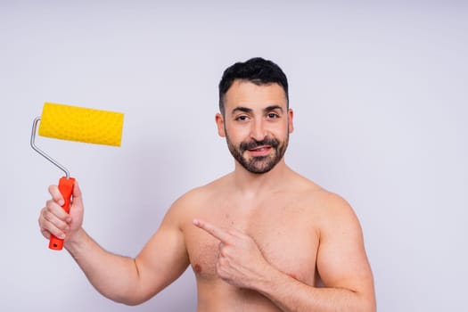 Cheerful young topless man hold paint roller isolated on a grey background studio.