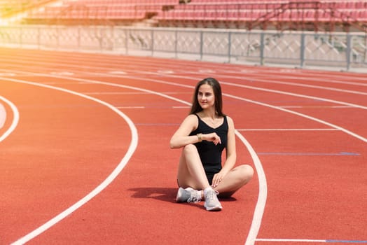A female coach with dark hair stands on the red running track of the stadium, dressed in sports uniform.
