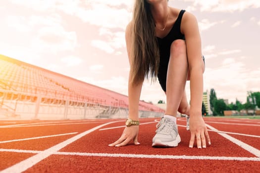 A female coach with dark hair stands on the red running track of the stadium, dressed in sports uniform.