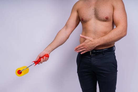 Cheerful young topless man hold paint roller isolated on a grey background studio.