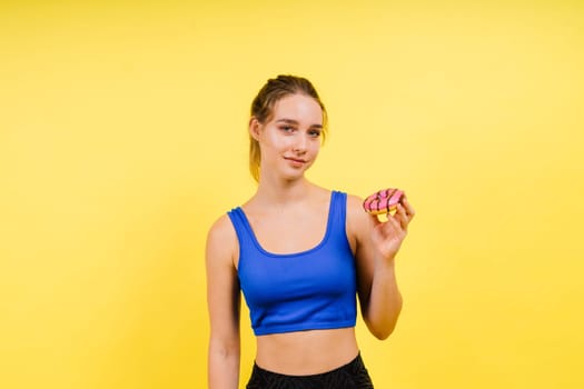 Lovely young caucasian woman in a sports wear with donuts on grey and yellow studio background.