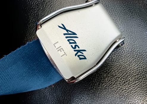 Anchorage, noc. 20 2023: Close-up view of a metallic safety belt buckle with the Alaska Airlines logo on a blue fabric background with a textured surface
