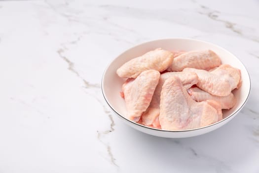 Raw chicken wings in white bowl, prepared for cooking on marble background