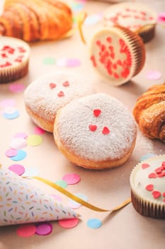 Berliner, cinnamon rolls and cupcakes for carnival and party. German Krapfen or donuts with streamers and confetti. Colorful carnival or birthday image