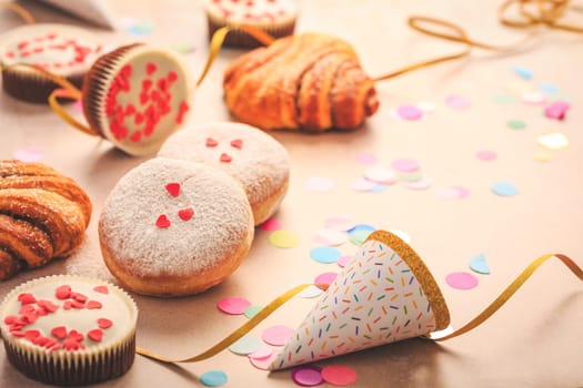 Berliner, cinnamon rolls and cupcakes for carnival and party. German Krapfen or donuts with streamers and confetti. Colorful carnival or birthday image