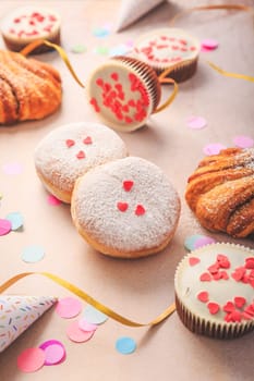 Berliner, cinnamon rolls and cupcakes for carnival and party. German Krapfen or donuts with streamers and confetti. Colorful carnival or birthday image