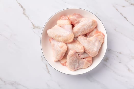 Raw chicken wings in white bowl, prepared for cooking on marble background