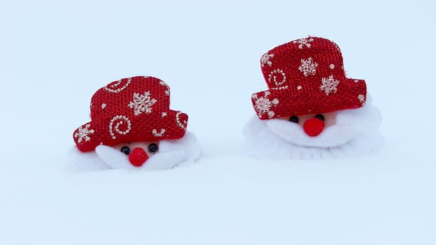 Two Christmas decorations of the head of Santa Claus on white snow