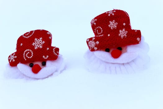Two Christmas decorations of the head of Santa Claus on white snow