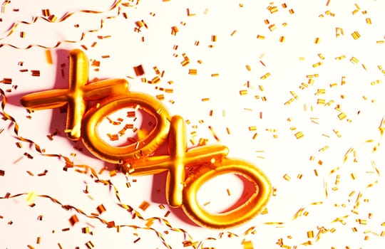 Golden xoxo foil balloon on pink background with gold glitter confetti. Top view. Valentine's day background. Celebration party romance dating special occasion greeting card.