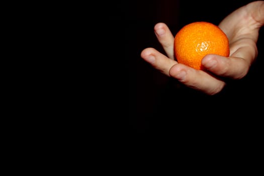 hand holds a orange on a black background