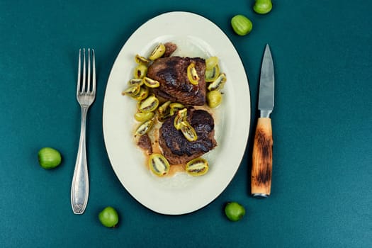 Roasted ostrich steak and mini kiwi on a plate