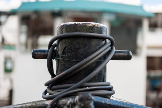 Close-up view of a black bollard of a cutter on the bow with folded power cables in front of the out-of-focus wheelhouse in the harbor of Leer in East Frisia.