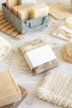 Organic handmade beige soap bar with blank label on soap saver bag near hygiene Items - natural sponges and brush, bamboo toothbrushes and cotton swabs, close up, mockup