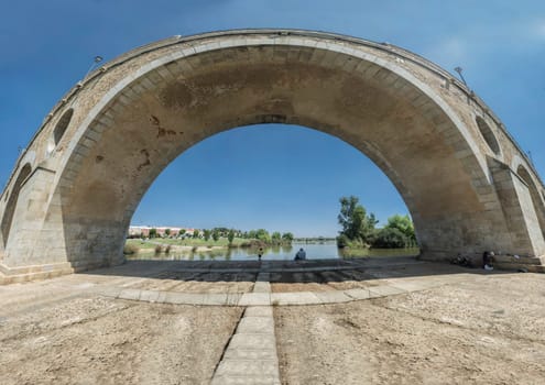 Fishers sitting under Puente de Palmas arch, Badajoz, Spain. Extra wide angle view