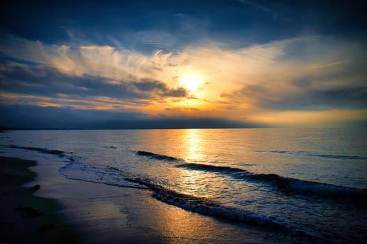 Sunset on the west beach on the Baltic Sea. Waves, beach, cloudy sky and the last rays of sunshine on the coast. Landscape photo