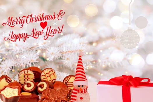 Merry Christmas and Happy New Year greeting card. Various chocolate candies sweets, a cute winter snowman and a gift package on table over abstract winter background.