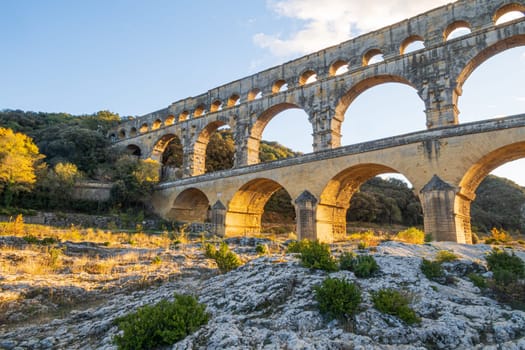 The magnificent Pont du Gard at setting sun. Ancient Roman three-tiered aqueduct bridge. Built in the 1st century AD to carry water to the Roman colony of Nemausus (Nîmes).  Photography taken in Vers-Pont-du-Gard, Provence, southern France.