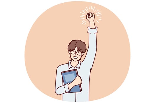 Joyful guy student with textbook in hand makes winning gesture feel happy after winning olympiad. Young man with book is satisfied with purchase of long-awaited book by favorite author